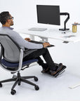 Person using a standing desk with a Humanscale FR500 black footrest in a modern office setting. Kansas City Office Design.
