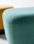 Two upholstered SitItOn Pasea Ottomans, one yellow and one teal, on a light gray surface. Kansas City Office Design.