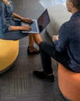Two people sitting on orange and yellow stools using laptops. Kansas City Office Design.