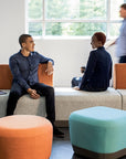 Two people sitting on a modern sofa with colorful SitOnIt Pasea ottomans in a bright room. Kansas City Office Design.