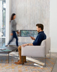 Man sitting on a modern SitOnIt Cameo Club chair in a stylish living room with a blurred woman walking by. Kansas City Office Design.