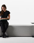 Person sitting on a modern gray sofa with adjustable Humanscale Float micro tables on a white background. Kansas City Office Design.