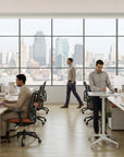 Modern office with large windows overlooking a cityscape, featuring employees at work. Kansas City Office Design