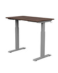 Back view of the SitonIt Switchback Height Adjustable Sit-to-Stand Desk. It has a Silver base with a 24"D x 42"W Walnut top - Kansas City Office Furniture