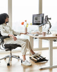 Person sitting at a modern desk with ergonomic chair and Humanscale footrest in a bright room. Kansas City Office Design.