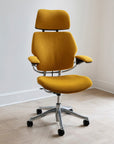 Yellow Humanscale Freedom office chair with a headrest on a wooden floor against a white wall. Kansas City Office Design.