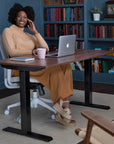 Woman sitting at a SitonIt Height Adjustable desk with a laptop and mug, surrounded by books in a home office setting. Kansas City Office Design.