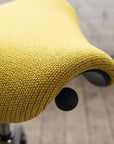Close-up of a yellow Humanscale saddle stool seat with a blurred background. Kansas City Office Design.