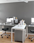 Modern office setup with two desks, Humanscale saddle stool, and computer monitors against a gray wall. Kansas City Office Design.