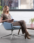 Woman sitting in a modern Gobi lounge chair in an office setting with plants and a desk. Kansas City Office Design.