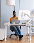 Person sitting at a desk with a laptop and computer monitor in a modern office setting. Kansas City Office Design.