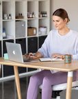 Woman sitting at a SitOnIt Reya desk with a laptop, notebook, and mug in a home office setting. Kansas City Office Design.