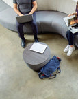 Two people sitting on a modern sofa with a round wooden table and a blue backpack on the floor. Kansas City Office Design.