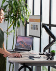 Woman using a laptop at a standing desk with a plant in the background. Kansas City Office Design.