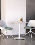 Modern white chairs with green seats around a small round table in a minimalistic setting. Kansas City Office Design