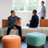 Two people sitting on a modern sofa with colorful SitOnIt Pasea ottomans in a bright room. Kansas City Office Design.