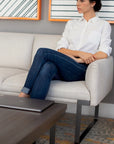 Woman sitting on a SitOnIt Cameo couch with a laptop on a coffee table in a modern living room. Kansas City Office Design