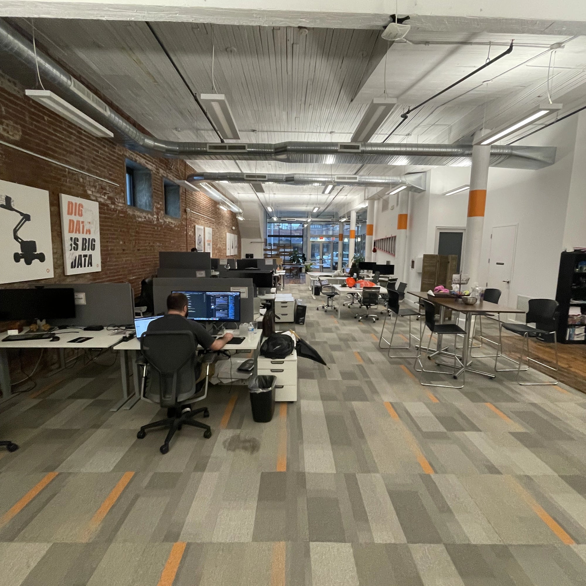 Modern office space with employees working at Sit to stand desks, colorful carpet, and exposed ceiling. Kansas City Office Design.