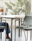 Woman sitting at a table with a cup, surrounded by modern chairs and plants. Kansas City Office Design.