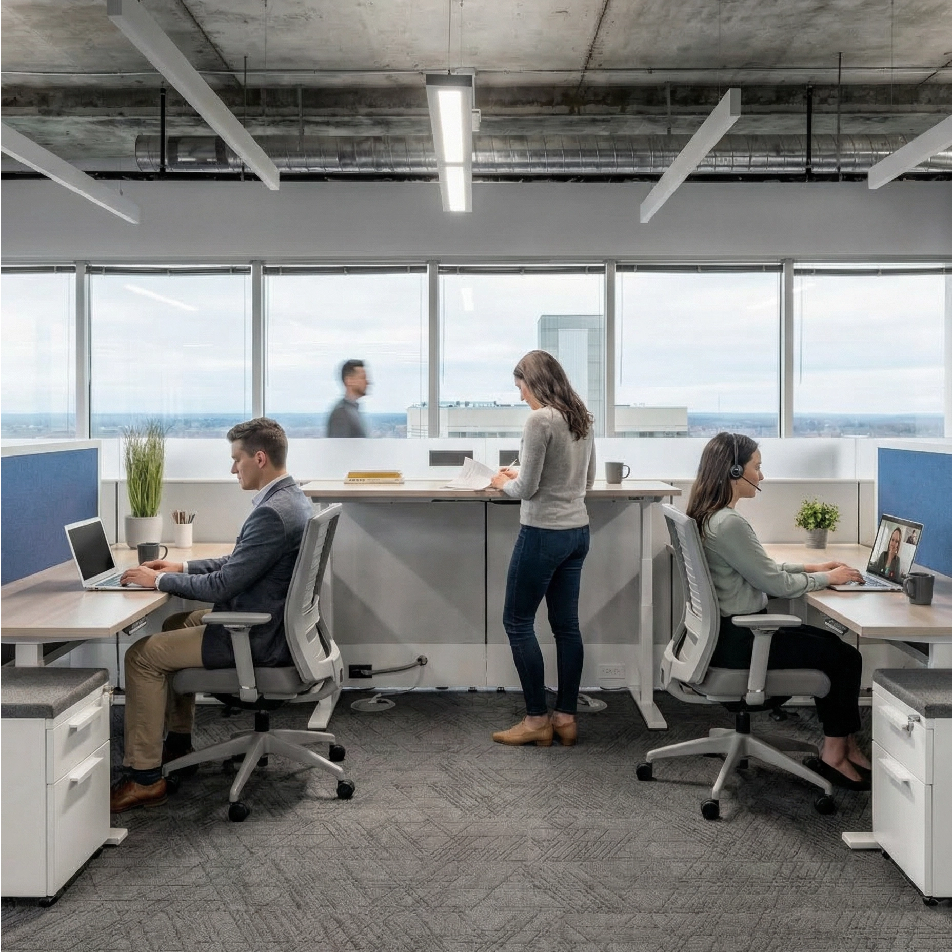 Modern office space with employees working at desks and a woman standing by a counter. Kansas City Office Design