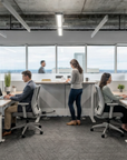 Modern office space with employees working at desks and a woman standing by a counter. Kansas City Office Design
