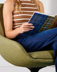 Person sitting in a green chair reading a book with a neutral background. Kansas City Office Design.