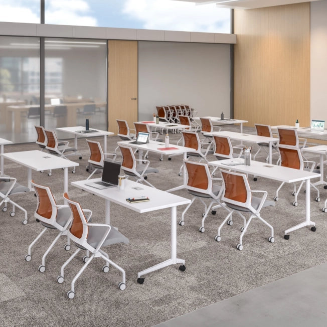 Modern office setup with white tables and orange chairs in a well-lit room. Kansas City Office Design.