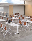 Modern office setup with white tables and orange chairs in a well-lit room. Kansas City Office Design.