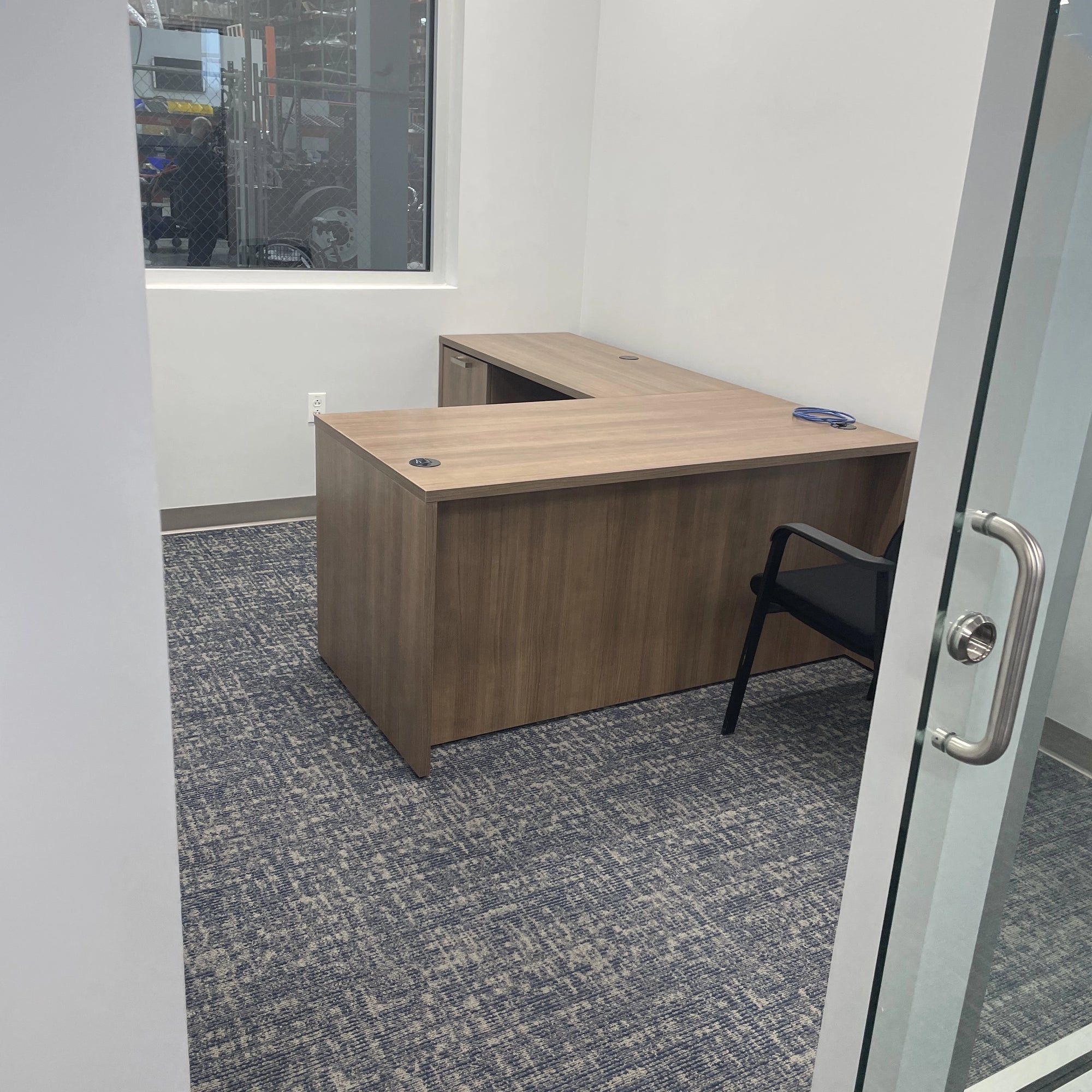 Wooden L-shaped desk in an office setting with a chair and glass door. Orange Ev. Kansas City Office Design.