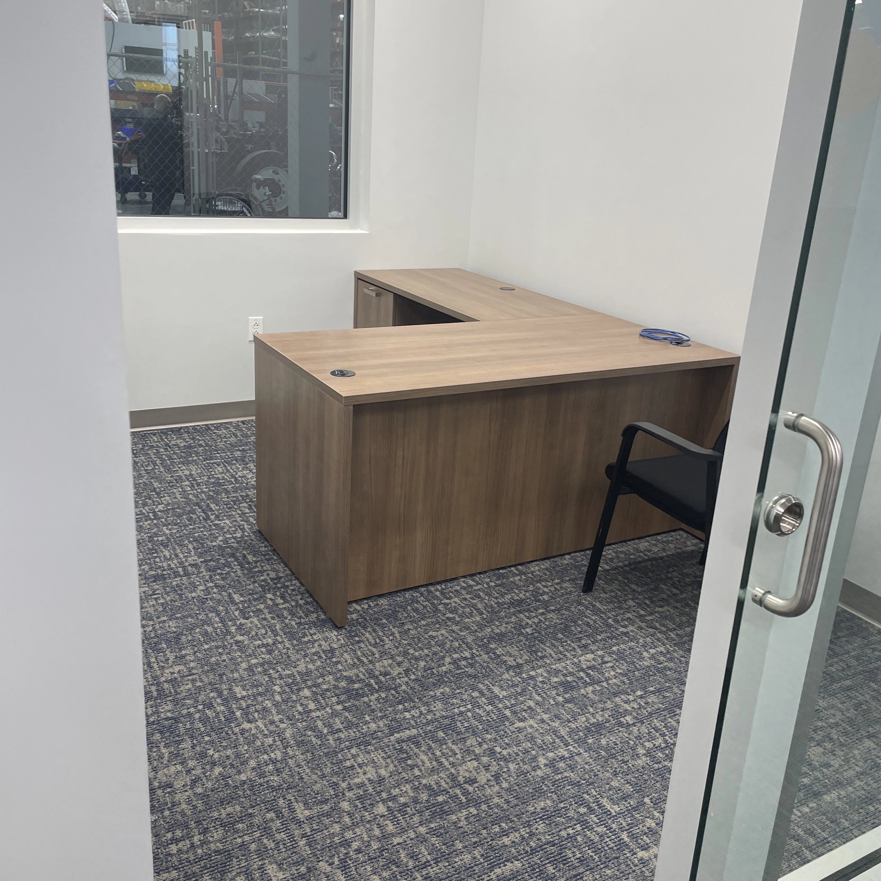 Wooden L-shaped desk in an office setting with a chair and glass door. Orange Ev. Kansas City Office Design.
