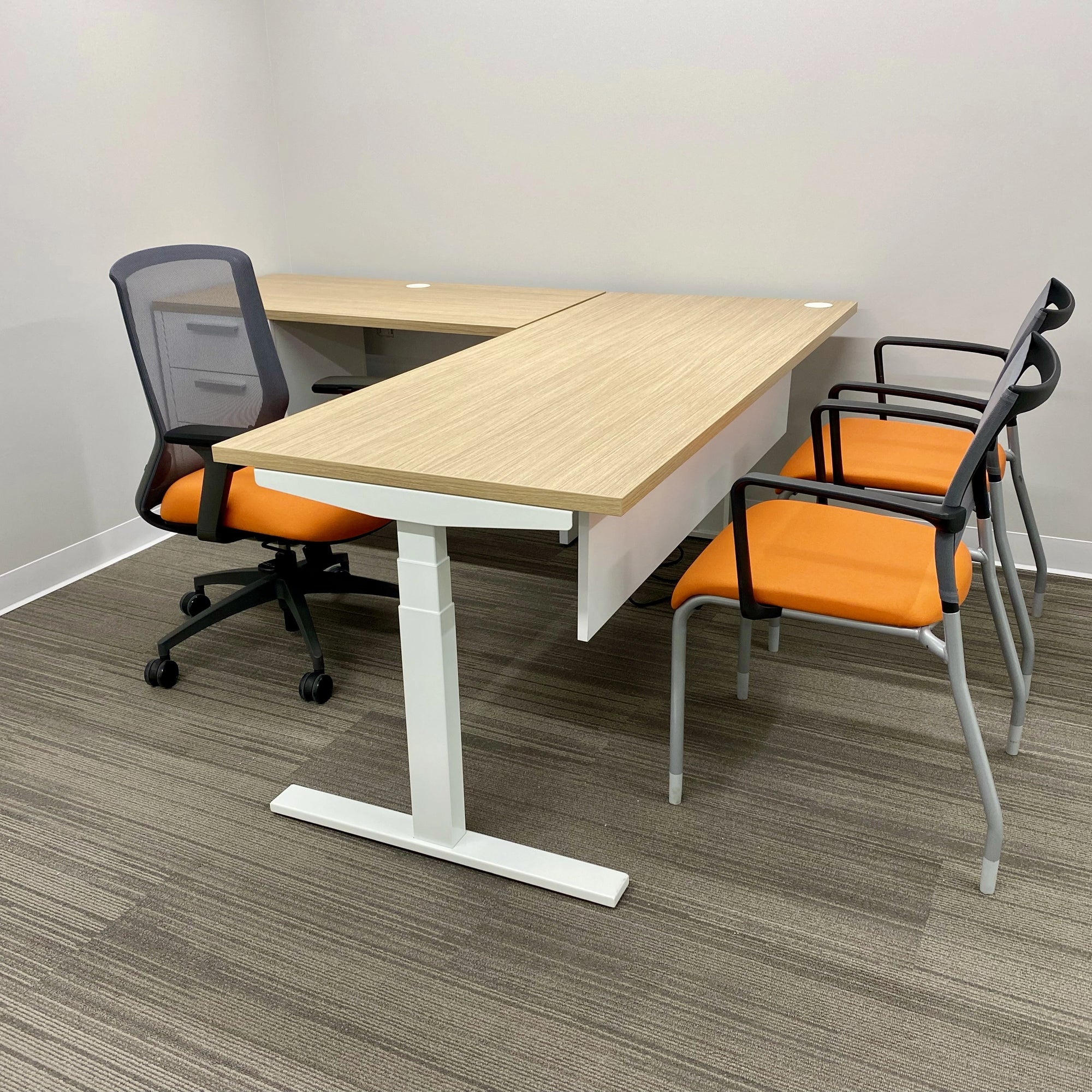 Modern office setup with a L-shaped sit to stand desk and orange chairs on a gray floor. Kansas City Office Design.