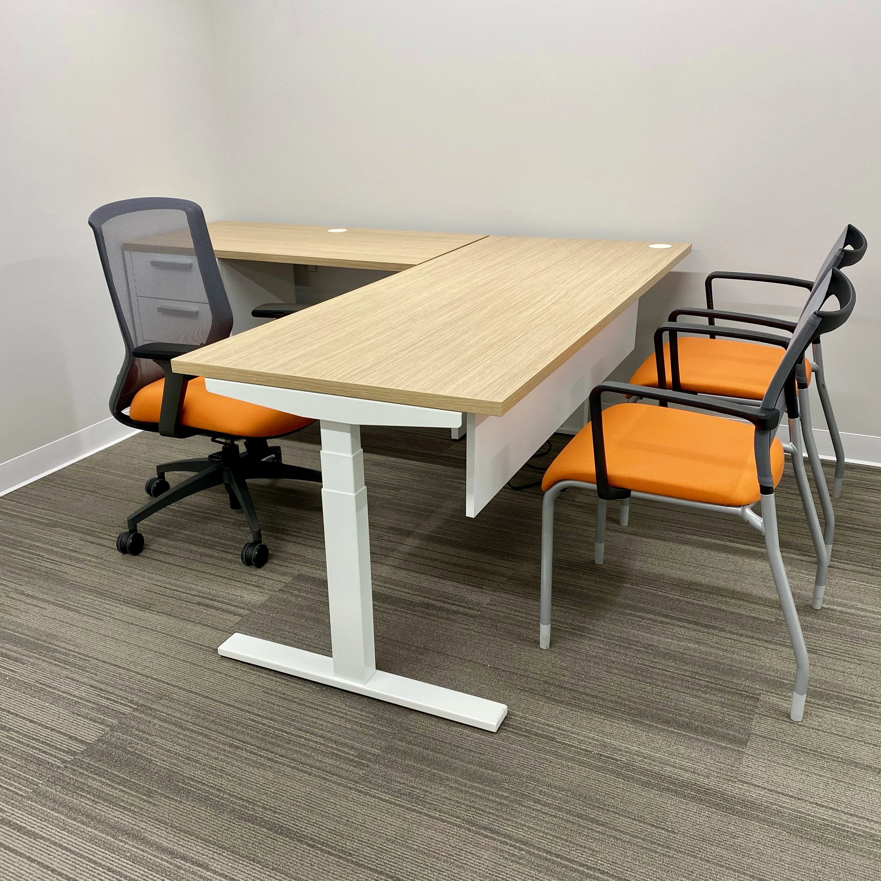 Modern office setup with a L-shaped sit to stand desk and orange chairs on a gray floor. Kansas City Office Design.