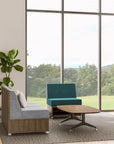 Modern office furniture with a blue chair, gray sofa, and coffee table in front of large windows with a view of greenery. Kansas City Office Design