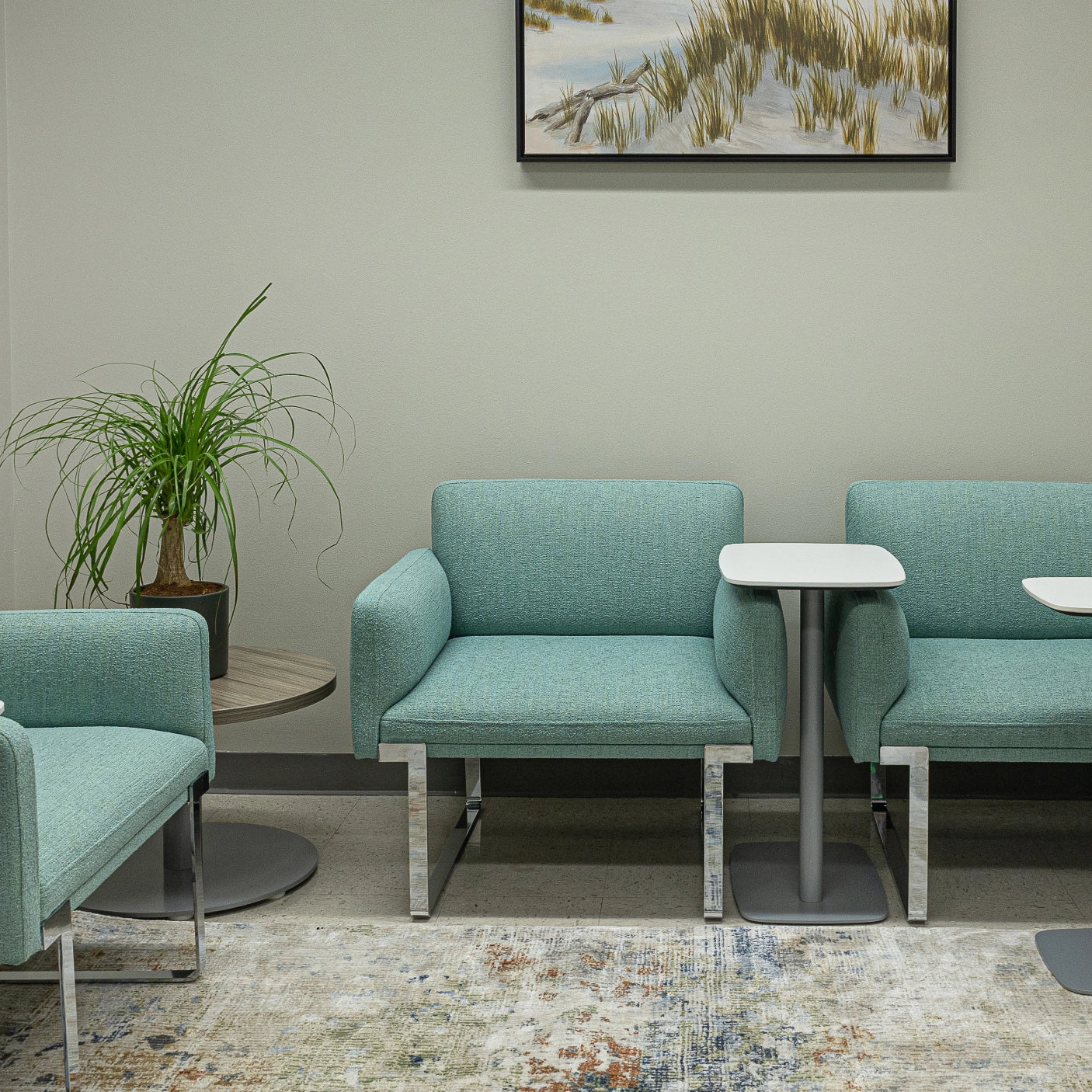 Modern waiting room with teal SitOnIt Cameo chairs and a small table, featuring a nature-themed painting on the wall. Kansas City Office Design
