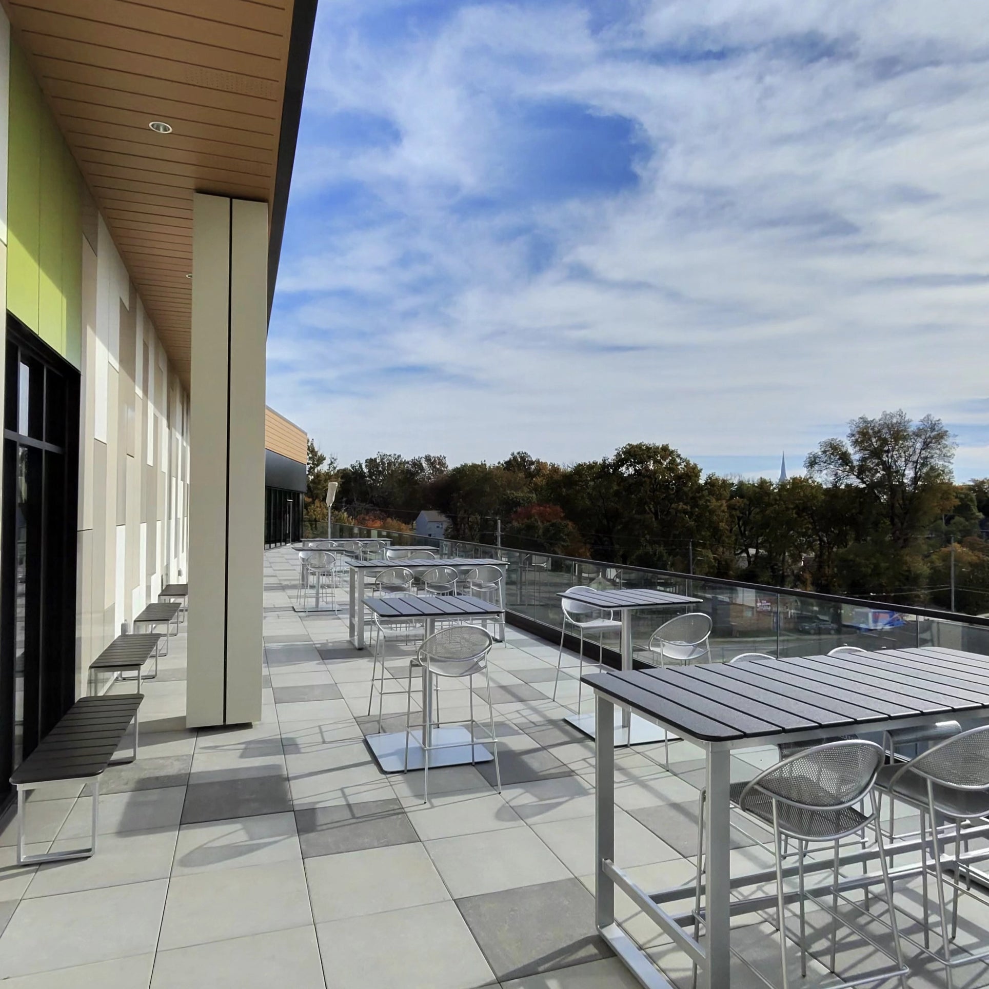 Outdoor seating area with tables and chairs on a rooftop deck, under a blue sky with clouds. Kansas City Office Design.