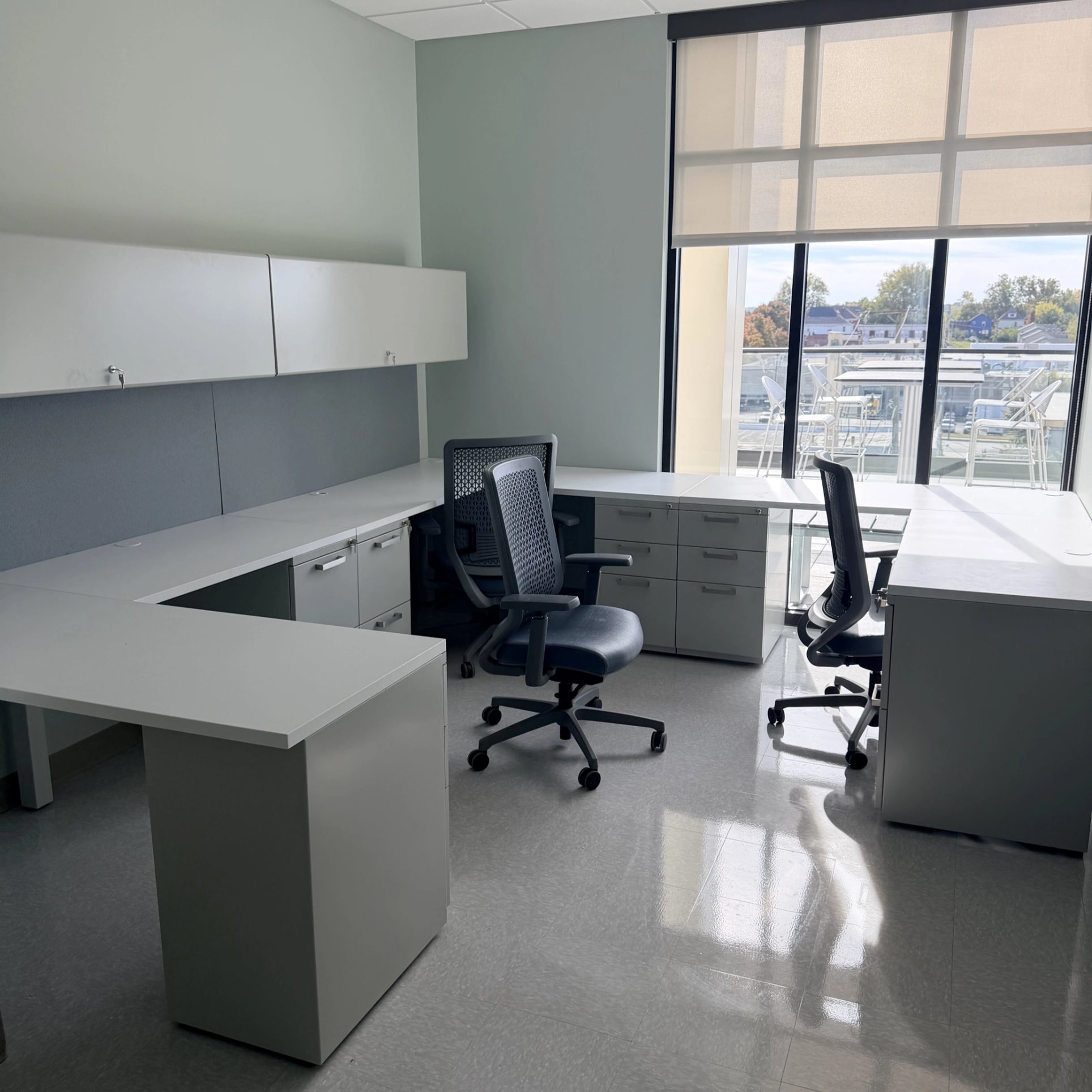 Modern office space with white desks and chairs near large windows. Kansas City Office Design.