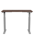 Front view of the SitonIt Switchback Height Adjustable Sit-to-Stand Desk. It has a Silver base with a 24"D x 48"W Walnut top - Kansas City Office Furniture