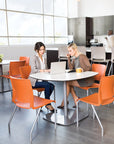 Two women sitting at a table in a modern office setting with orange chairs. Kansas City Office Design.