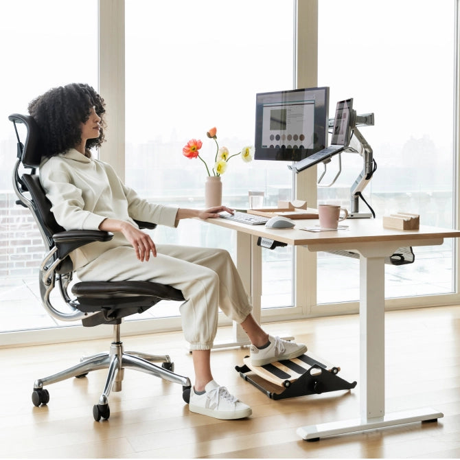 Person sitting at a modern desk with ergonomic chair and Humanscale footrest in a bright room. Kansas City Office Design.