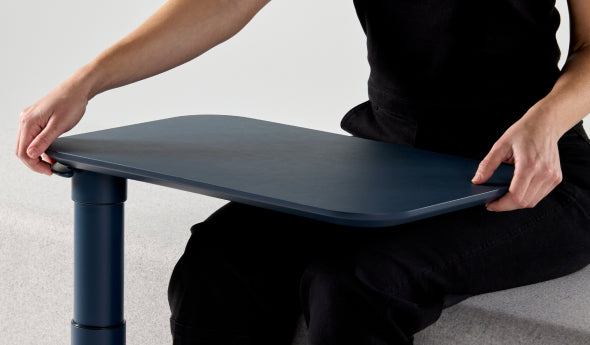 Person adjusting a slate blue adjustable Humanscale Float micro desk on a light gray background. Kansas City Office Design.