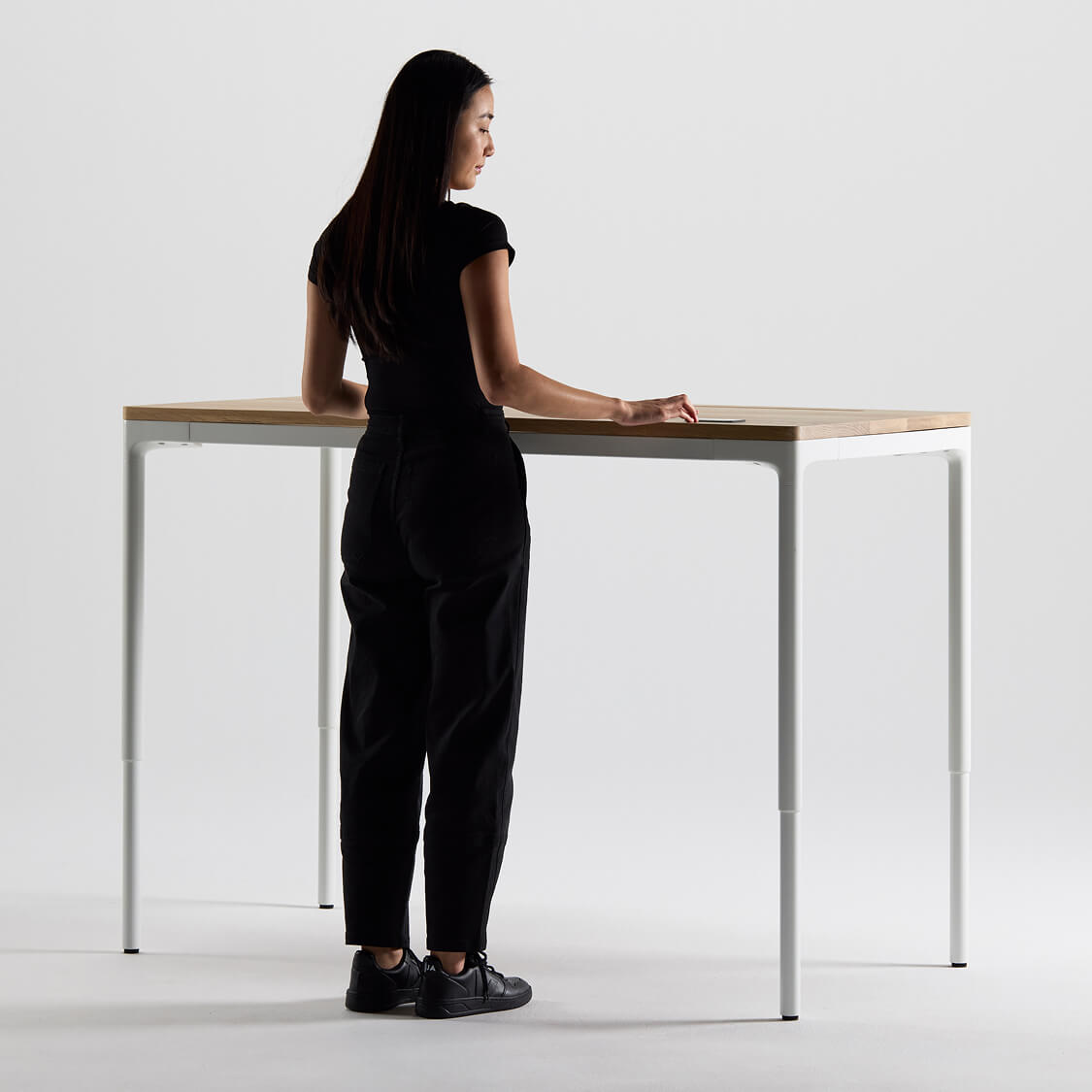 Woman in black outfit standing at a modern Humanscale eFloat Quattro standing desk with a white background. Kansas City Office Design.