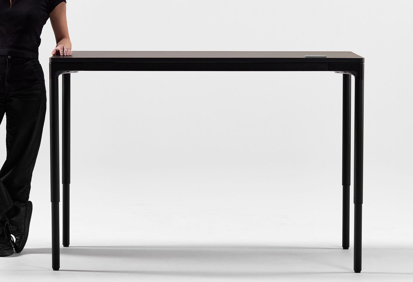 Person standing next to a black Humanscale eFloat Quattro table on a white background. Kansas City Office Design.