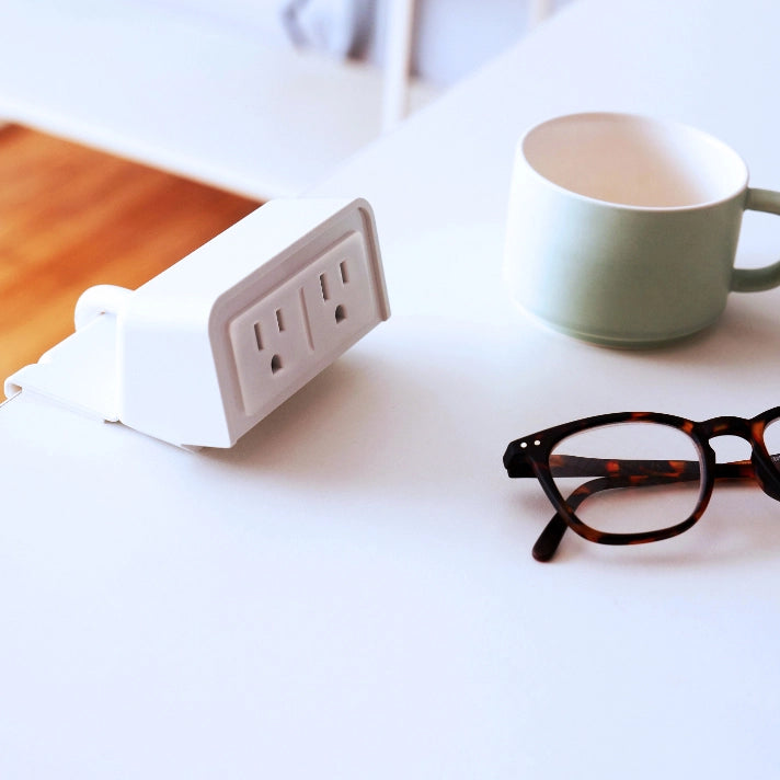 SitOnIt clamp on EON Power with dual outlets on a desk next to a mug and glasses. Kansas City Office Design.