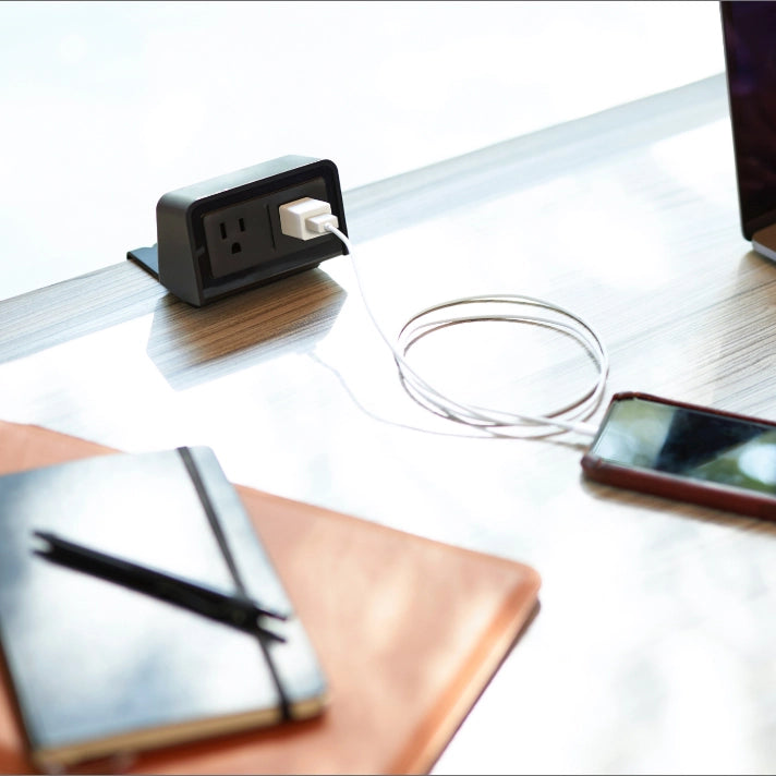 Black Dual outlet EON power on a white surface, with a phone and notebook in the foreground. Kansas City Office Design.