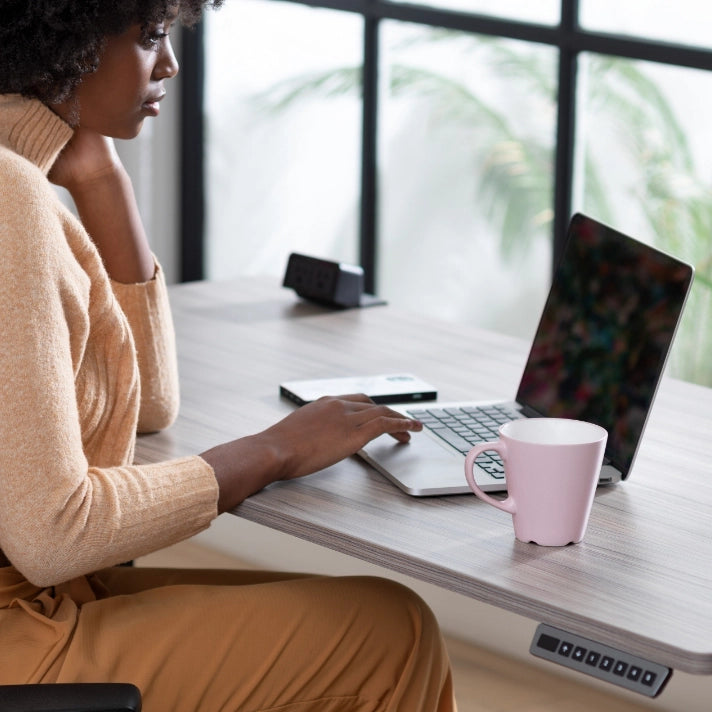 Person using a laptop with a pink mug on a desk in a bright room. Kansas City Office Design.