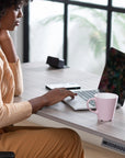 Person using a laptop with a pink mug on a desk in a bright room. Kansas City Office Design.