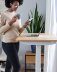 Woman using a smartphone next to a standing desk with a laptop and plant in a home office setting. Kansas City Office Design.