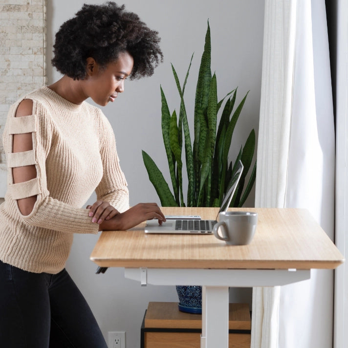 Woman using a laptop at a standing desk with a plant in the background. Kansas City Office Design.