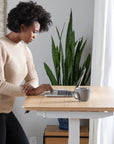 Woman using a laptop at a standing desk with a plant in the background. Kansas City Office Design.