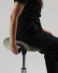 Person sitting on a modern green Humanscale saddle stool with a plain background. Kansas City Office Design.
